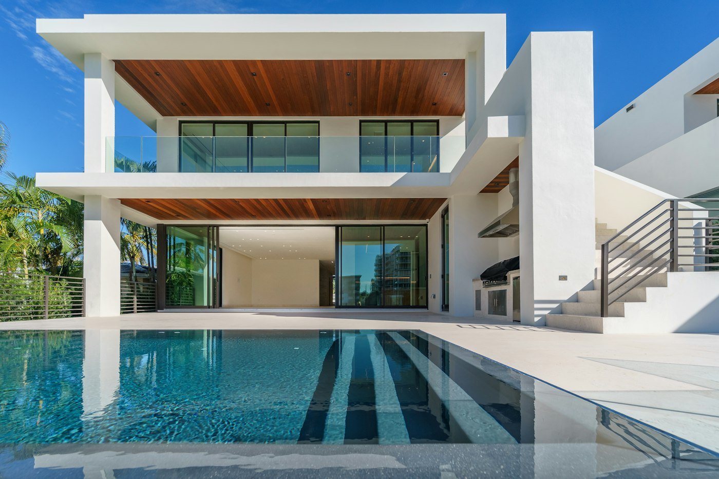 Residencia blanca de dos niveles con alberca, terrazas de madera y ventanales